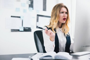 Genç sarışın güzel kadın menajer modern ofisinde çalışıyor elinde kalem tutarken kızgın, çoklu görev, iş konsepti gibi görünüyor..