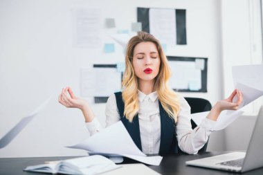 Kırmızı rujlu genç sarışın kadın menajer modern ofisinde çalışıyor. Huzurlu yoga pozisyonu ve vücut dili kavramında rahat görünüyor..