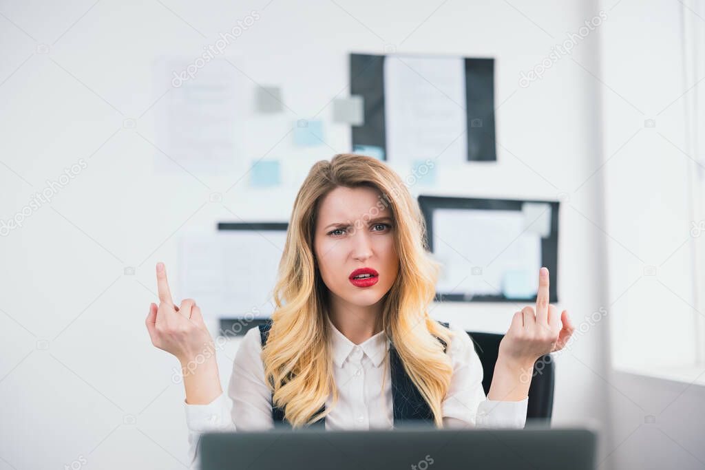 young beautiful businesswoman manager with red lipstick works in her modern office, looks angry showing fuck off sign with bith hands, body language concept.
