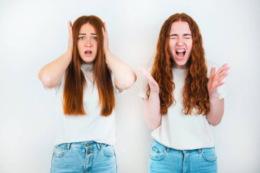 İzole edilmiş beyaz arka planda duran iki kızıl saçlı genç kadın, biri yüksek sesle bağırıyor, diğeri kulaklarının yanında el ele tutuşuyor, vücut dili kavramı..