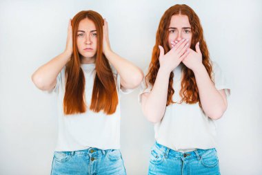 İzole edilmiş beyaz arka planda duran iki kızıl saçlı genç kadın, biri elleriyle yüzünü kapatıyor, diğeri de kulaklarının yanında el ele tutuşuyor, vücut dili kavramı..