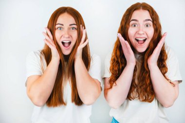 Yüz yüze el ele tutuşan iki kızıl saçlı genç kadın şaşırmış görünüyor, izole edilmiş beyaz arka plan üzerinde duruyorlar, vücut dili kavramı.