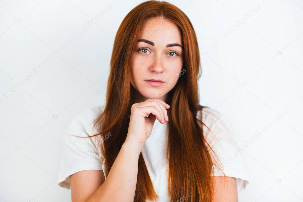 portrait of redheaded young woman looking natural holding hand near her chin on isolated white backgroung, style and beauty concept.