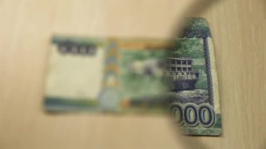 Masada elinde büyüteçle duran 2000 Lao Kip banknotuna bakın. İş ve finans kavramı. ters taraf