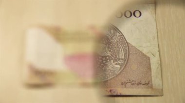 Masada elinde büyüteçle duran beş bin İran riyal faturasını izleyin. İş ve finans kavramı. ters taraf