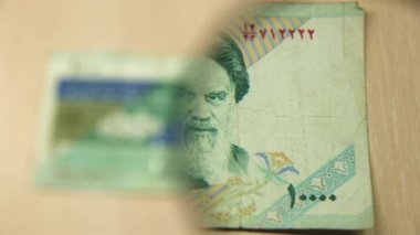 Masada elinde büyüteçle duran 10 bin İran riyal faturasını izleyin. İş ve finans kavramı. Obverse