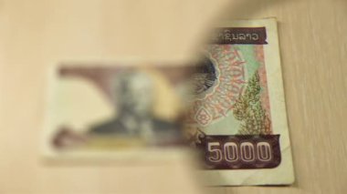 Beş bin Lao Kip banknotunun büyüteçle masada yattığını görün. İş ve finans kavramı. Obverse