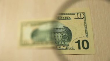 Masada elinde büyüteçle duran 10 Amerikan Doları banknotuna bakın. İş ve finans kavramı. ters taraf