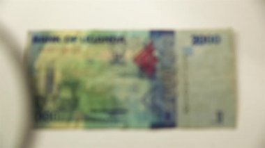 İki bin Ugandalı şilin ve bir büyüteç. Bir kağıt faturayı büyüteçten izle. Obverse.