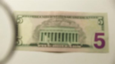 Beş Amerikan doları ve bir büyüteç. Bir kağıt faturayı büyüteçten izle. ters.