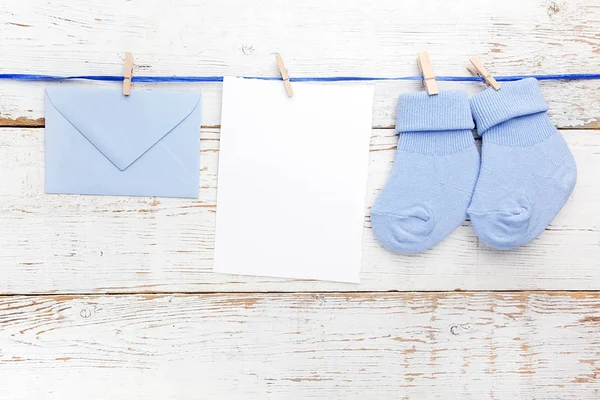 Chico pequeño calcetines azules, tarjeta en blanco y evelop sobre fondo de madera blanca. Puesta plana . — Foto de Stock