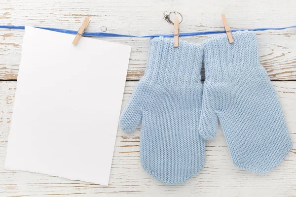 Piccoli guanti per bambini, carta bianca su sfondo bianco in legno. Piatto. Vista dall'alto — Foto Stock