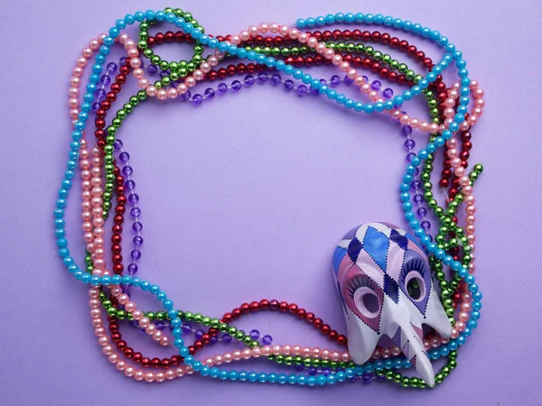 Mardi Gras kralen en masker maken van een frame met kopie ruimte op paarse achtergrond. Flat lag. Bovenaanzicht — Stockfoto