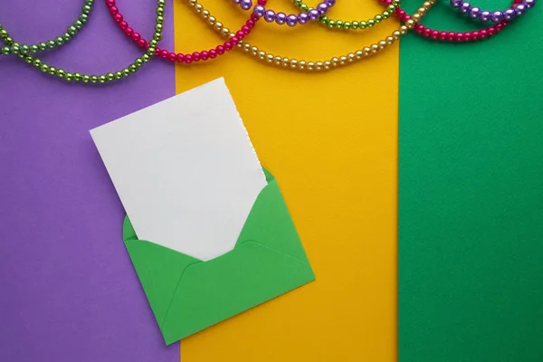 Cuentas Mardi Gras multicolor y sobre con tarjeta sobre fondo de papel. Vista superior — Foto de Stock