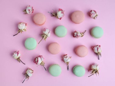 Fransız tatlı macarons pembe bir arka plan üzerinde kuru gül çiçek desenle. Düz yatıyordu