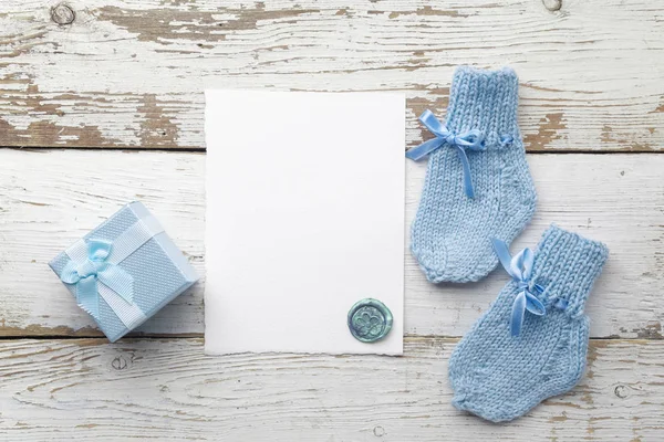 Hermoso regalo, calcetines babys y postal en blanco sobre fondo de madera blanca. Puesta plana —  Fotos de Stock