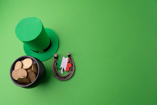 Happy St Patricks Day leprechaun hat with gold coins and lucky charms on green background. Top view.