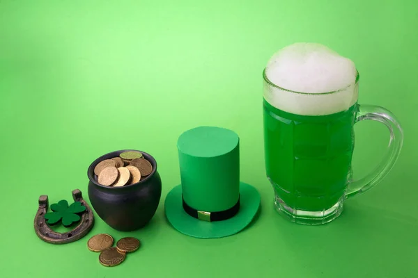 St Patricks Day cerveja verde com trevo, panela com moedas de ouro, ferradura e chapéu Leprechaun contra fundo verde . — Fotografia de Stock