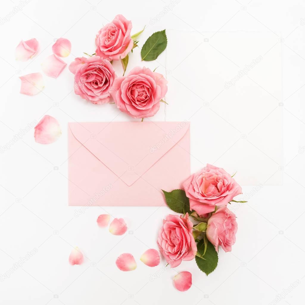 Envelop with white card and rose background. Top view. Flat lay