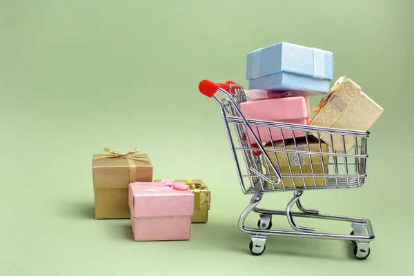 Caixa de presentes coloridos, carrinho de compras de supermercado em fundo verde — Fotografia de Stock