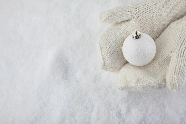 Juldekoration bollen i snöiga händer i vantar på snö — Stockfoto