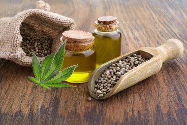 Tahta kaşıkta kenevir tohumu, cam kavanozda yağ, ahşap zeminde yeşil yaprak kenevir.