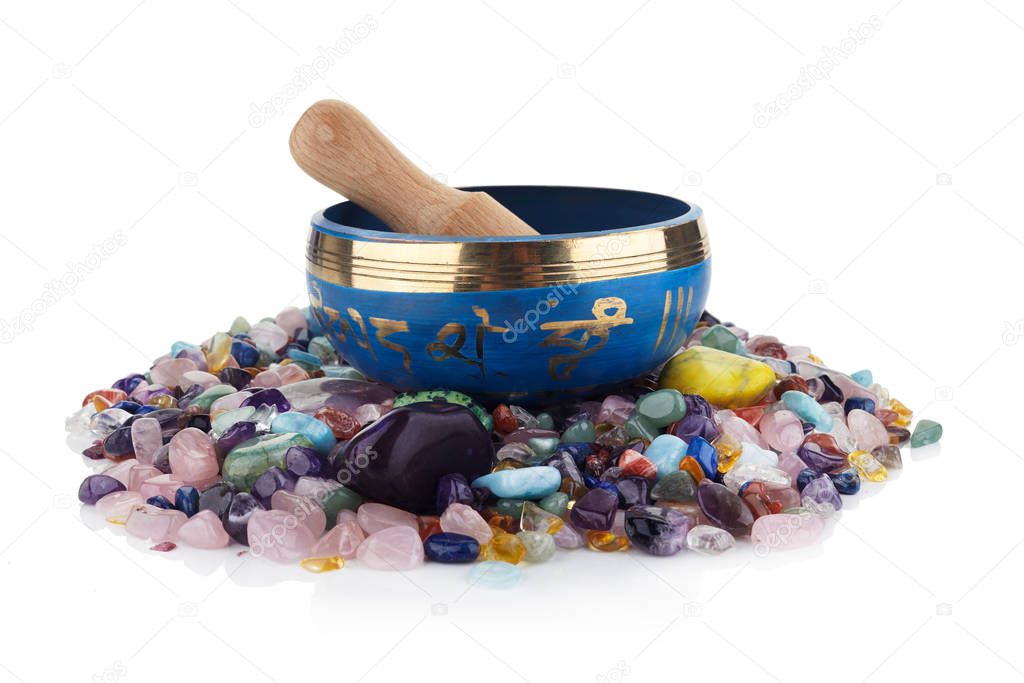 tibetan singing bowl and multicoloured healing chakra stones against a white background