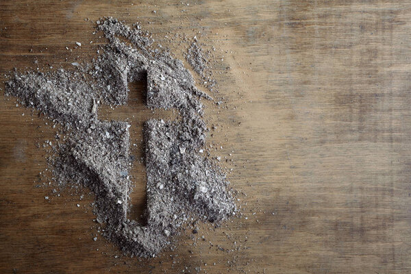 Christian cross symbol made of ash on a wooden background