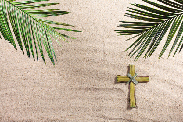 Cross and Palm Tree Leaves on sand. Palm sunday concept. Top view
