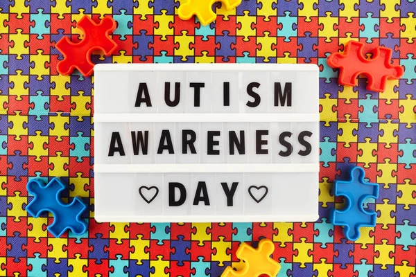 Light box with World autism awareness day text on colored puzzle background. Top view — Stock Photo, Image