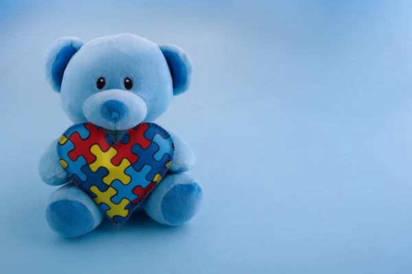 World Autism Awareness, conceito com ursinho de pelúcia segurando quebra-cabeça ou padrão de quebra-cabeça no coração no fundo azul — Fotografia de Stock