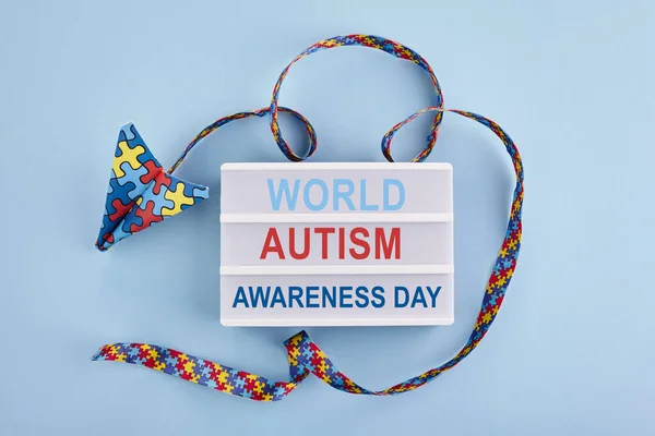 Autism awareness day or month. Paper plane in origami style with autism awareness puzzle ribbon on blue background. — Stock Photo, Image