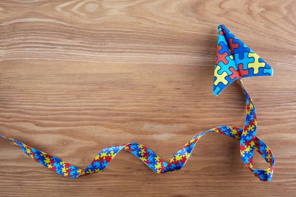 Consciência de autismo dia ou mês. Plano de papel no estilo origami com fita de quebra-cabeça de consciência de autismo em fundo de madeira . — Fotografia de Stock