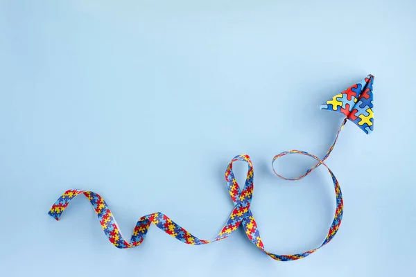 Autisme bewustzijn dag of maand. Papier vliegtuig in origami stijl met autisme bewustzijn puzzel lint op blauwe achtergrond. — Stockfoto