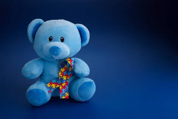 World Autism Awareness, концепция с плюшевым медведем, держащим ленту с рисунком на голубом фоне — стоковое фото