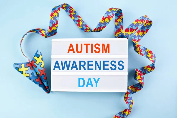 Autism awareness day or month. Paper plane in origami style with autism awareness puzzle ribbon on blue background. — Stock Photo, Image