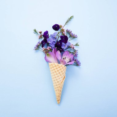 Mavi arka planda düz stil waffle 'lı mor çiçekler. Flatlay, üst manzara. Doğum günü, bahar arkaplanı.