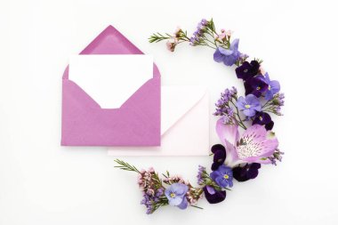 Yaratıcı iş tasarımı için beyaz arka planda mor kır çiçekleriyle dolu boş beyaz tebrik kartı ve zarf. Düz yatıyordu