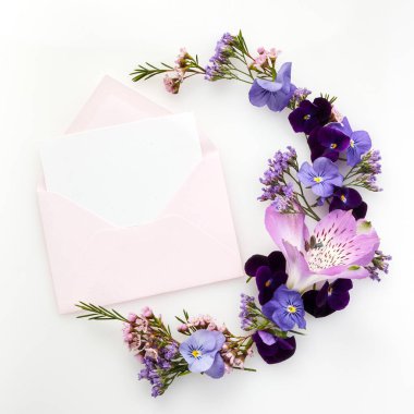 Yaratıcı iş tasarımı için beyaz arka planda mor kır çiçekleriyle dolu boş beyaz tebrik kartı ve zarf. Düz yatıyordu