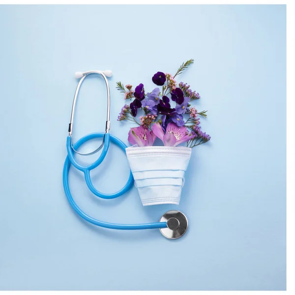 Blommor med mask och stetoskop pÃ ¥blÃ ¥bakgrund. Glad sjuksköterska dagskoncept. Ovanifrån — Stockfoto