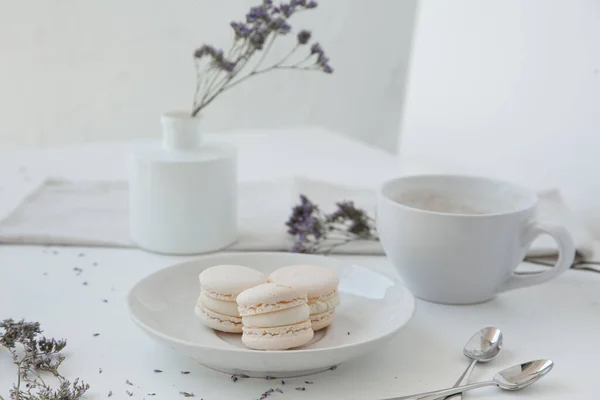 Macarons, café du matin sur table lumineuse avec vase flou et fleurs bleues sur fond Images De Stock Libres De Droits