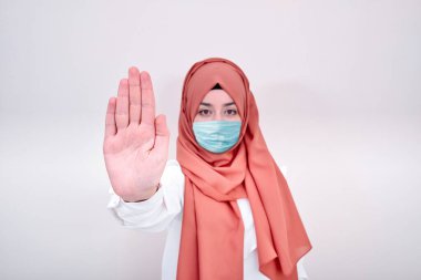 Korunmak için cerrahi maske takan Müslüman bir kız. Başörtülü kadın bir maske al ve dur tabelasını eline al.