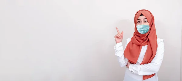 Korunmak için cerrahi maske takan Müslüman bir kız. Başörtülü kadın bir maske al ve mesaj alanına parmağıyla işaret et