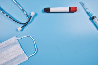 Tıp ya da sağlık endüstrisi kavramı. İzole edilmiş mavi yüzeyde şırınga, steteskop, kan tüpü ve yüz maskesi.