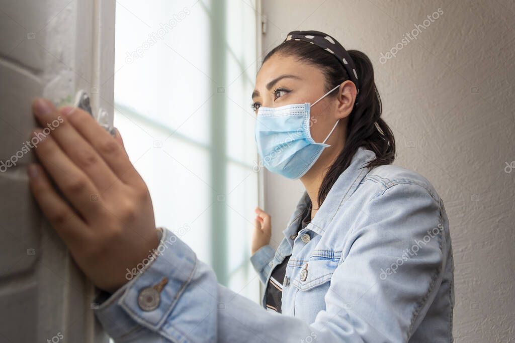 Mexican Latin woman standing with her hands on the door anxious to leave during confinement due to the Covid-19 health contingency