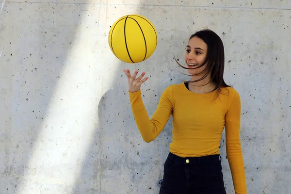Young girl and beautiful basketball player dressed in yellow doing tricks with yellow basketball in an urban court.