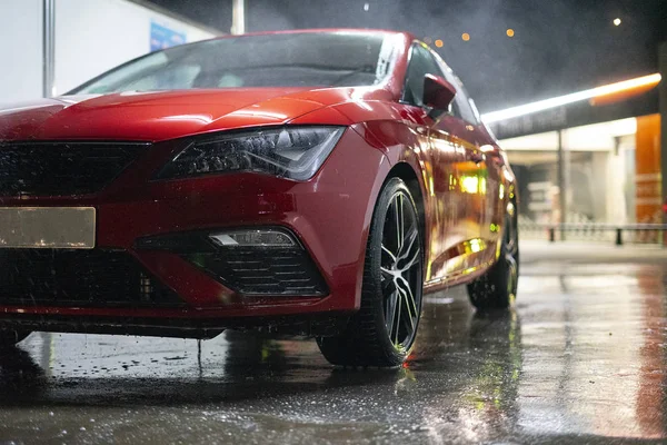 Red car in the rain at night.