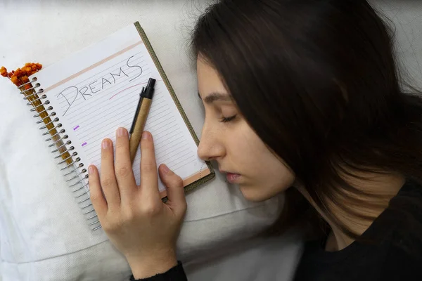 Notebook with the word Dreams written, next to a sleeping woman. Dreams Concept.
