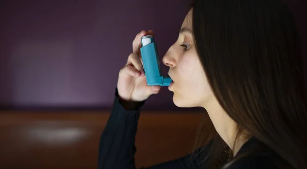 Woman inhaling a blue asthma inhaler at home. Asthma and coronavirus concept.