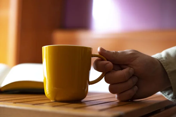 Hand picking up a yellow cup of coffee at home. Coffee in bed concept.